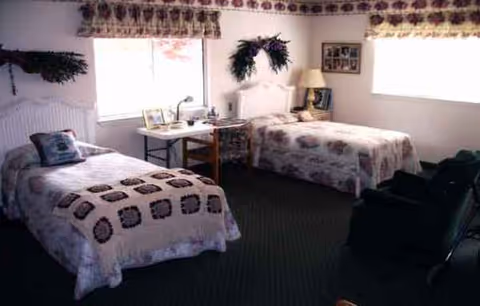 Meadowview Manor bedroom with two beds, floral quilts, desk, and decorative greenery.