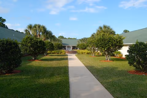 Exterior view of Pelican Garden senior living facility with a central walkway and manicured landscaping.