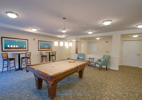 Well-lit interior recreation room with a pool table, bar-height tables and chairs, and lounge seating.