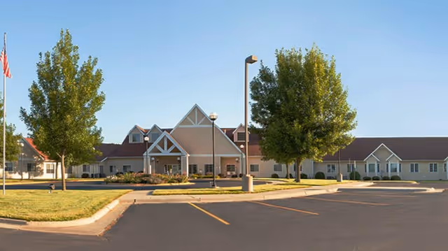Exterior view of Sanford Health Dell Rapids Orchard Hills facility with a large parking lot in front, green trees, and a clear blue sky.