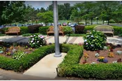 Landscaped outdoor courtyard with walking paths, trimmed hedges, flowering beds, three wooden benches and a central pole.