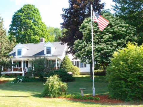 Front view of Fox Meadow Retirement Home with flagpole, trees, and a manicured lawn.