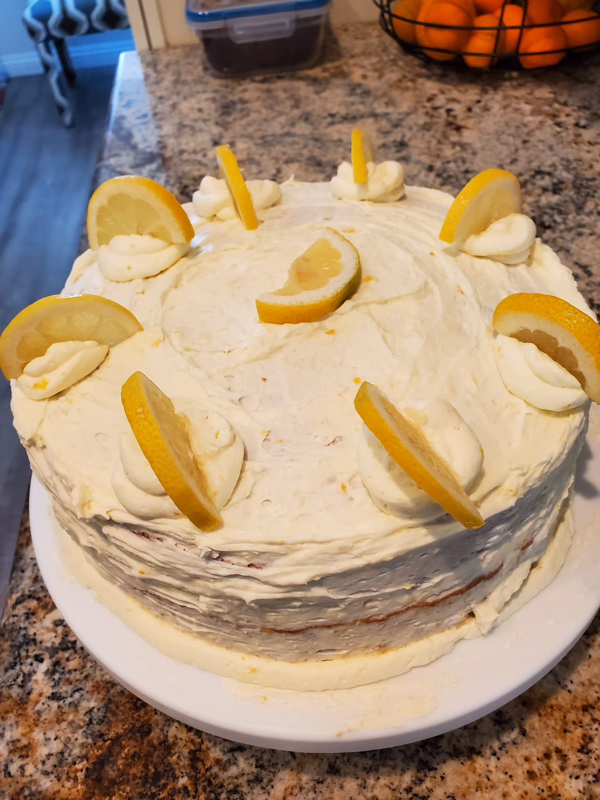 Round lemon-frosted layer cake topped with lemon slices on a kitchen countertop.