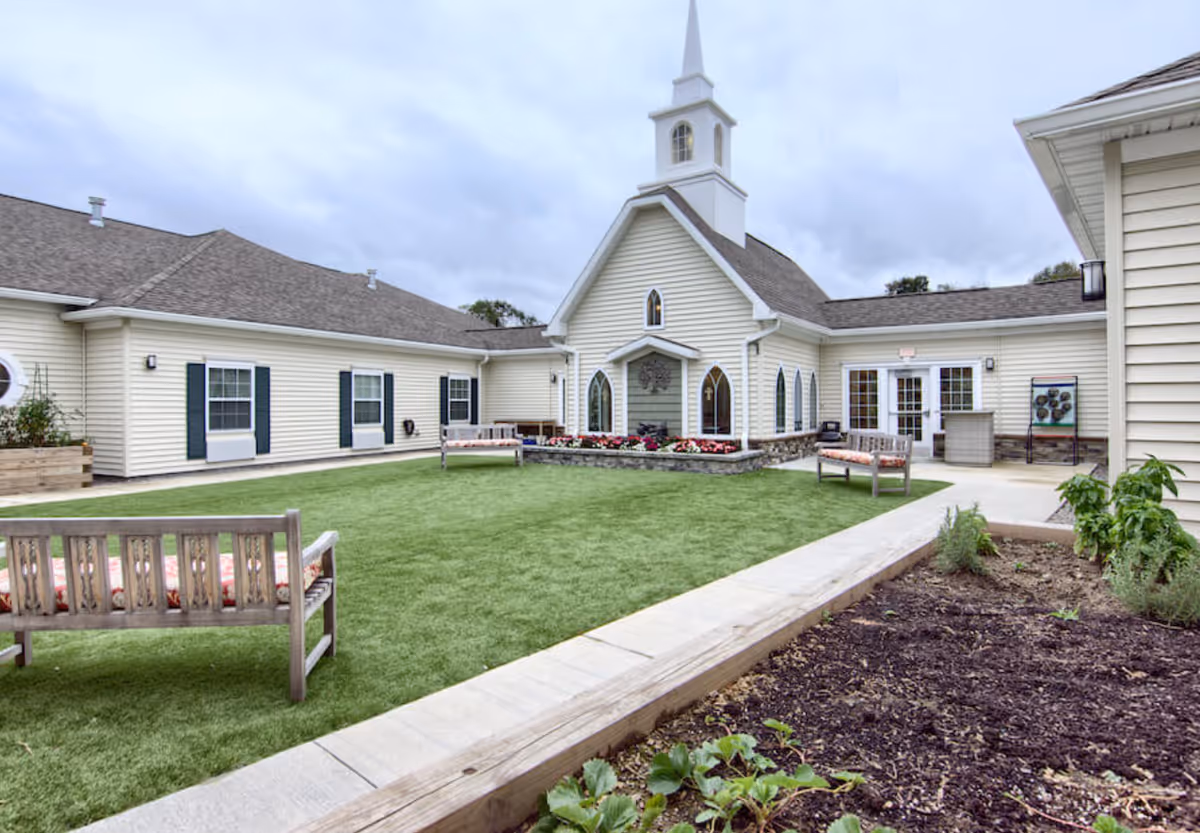 Landscaped courtyard with benches, artificial turf and a chapel-like senior living building with a steeple.