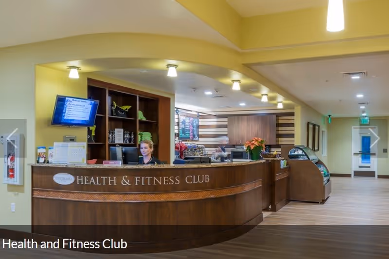 Interior view of a Health & Fitness Club reception desk with a staff member behind the counter in a senior living facility.