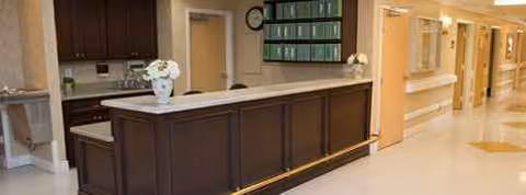 Dark wood front desk with marble top and flowers in Vista Manor Nursing Center lobby.