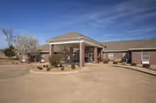 Brick single-story nursing center building with a covered portico entrance and circular driveway under a blue sky.
