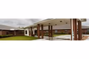 Exterior view of Renaissance Care Center showing a covered entrance with brick pillars and a driveway, with a grassy area and cloudy sky in the background.