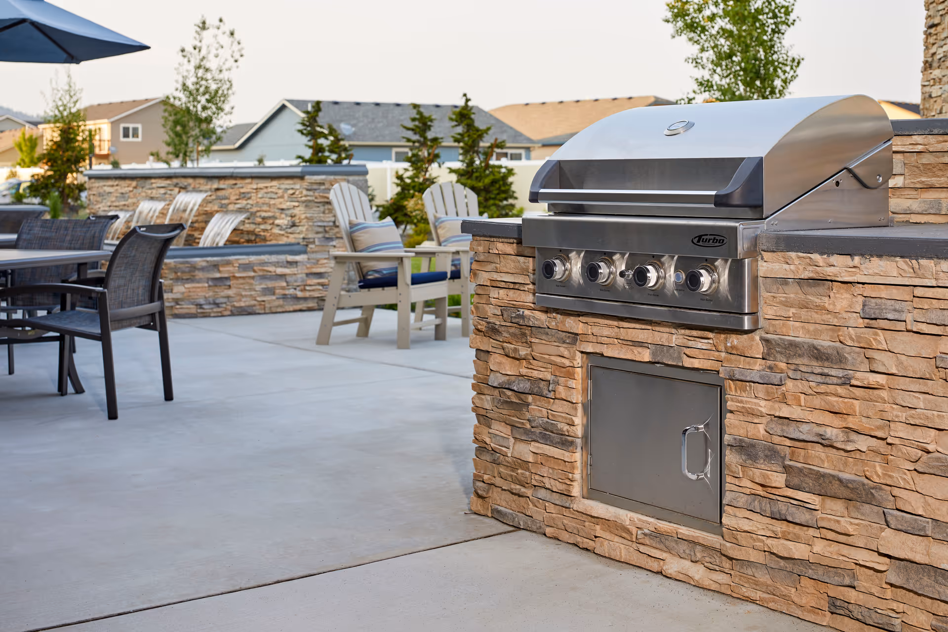 Outdoor patio area featuring a built-in stainless steel grill set into a stone counter with nearby tables and chairs.