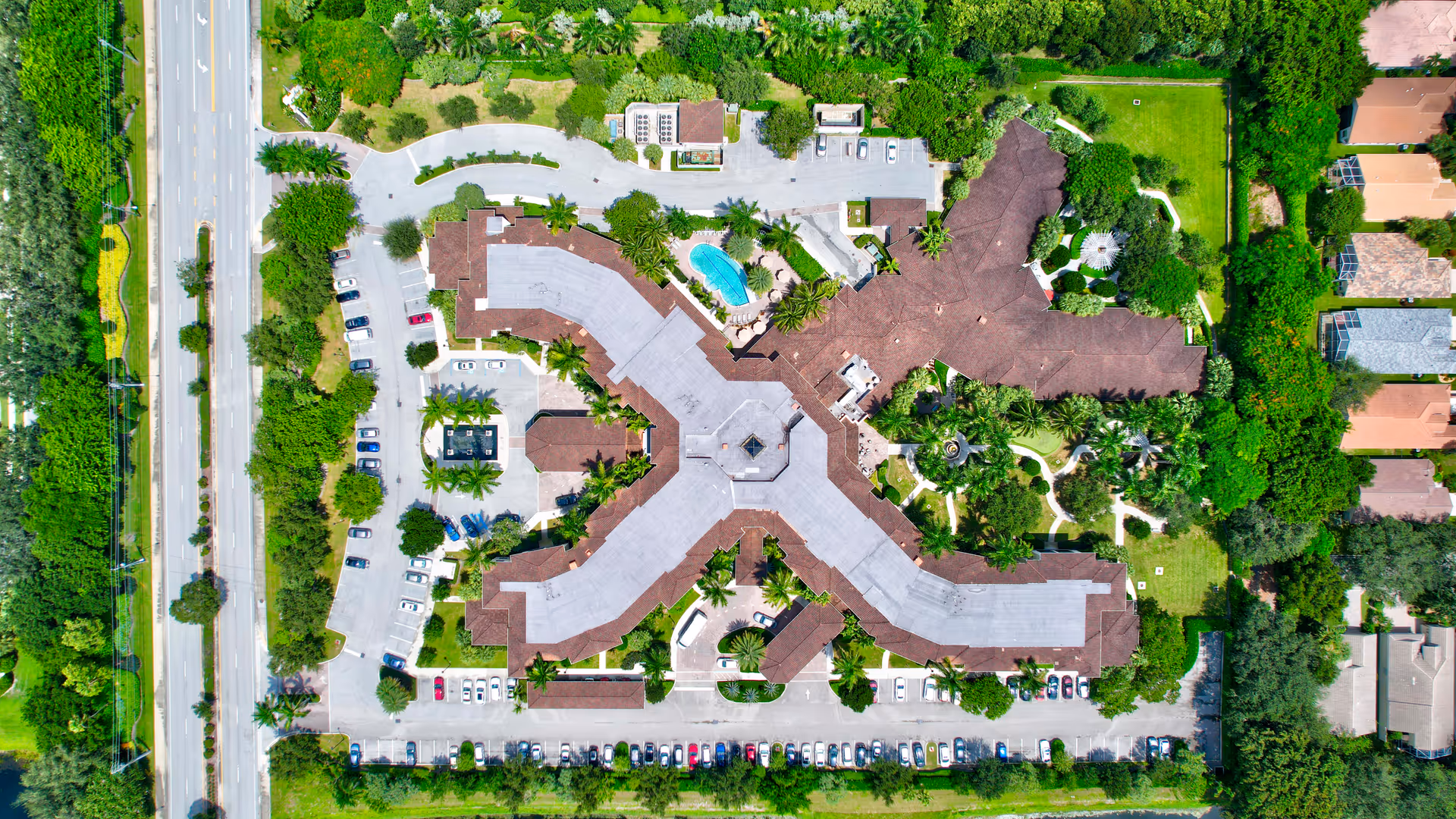 Aerial view of Allegro Senior Living facility in Boynton Beach, FL, showing a large building with multiple wings, surrounded by greenery, parking lots with cars, a swimming pool, and nearby roads.