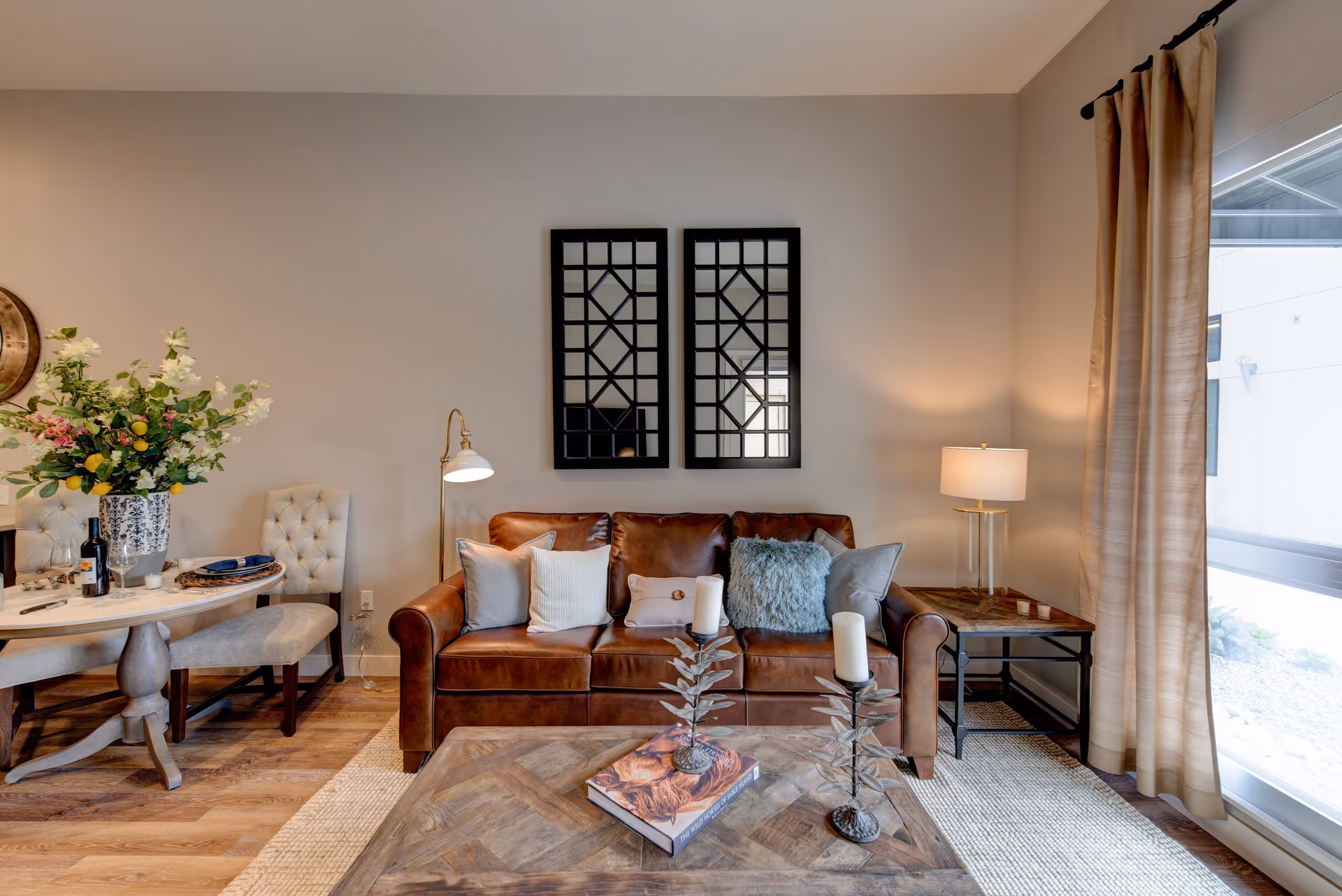 Cozy living room with a brown leather sofa, decorative pillows, a wooden coffee table, lamps, and a small dining nook to the left.