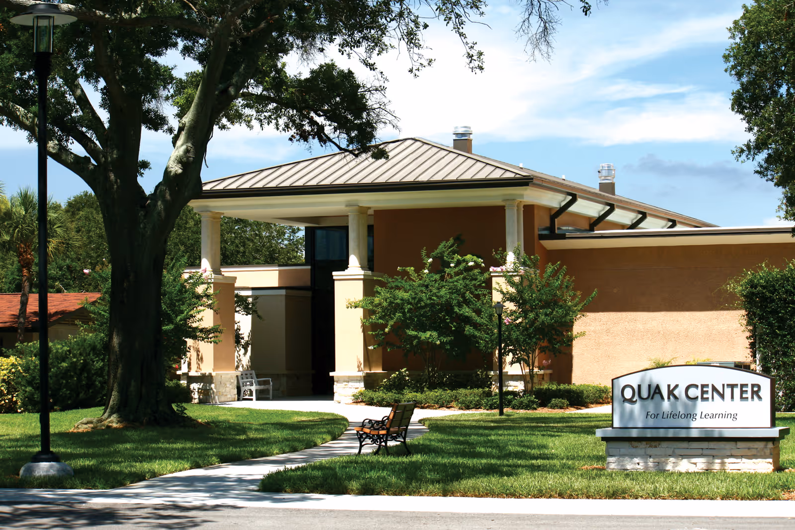 Front exterior of the Westminster Suncoast Quak Center with a covered entrance, trees, walkway, benches, and a sign reading 'QUAK CENTER'.