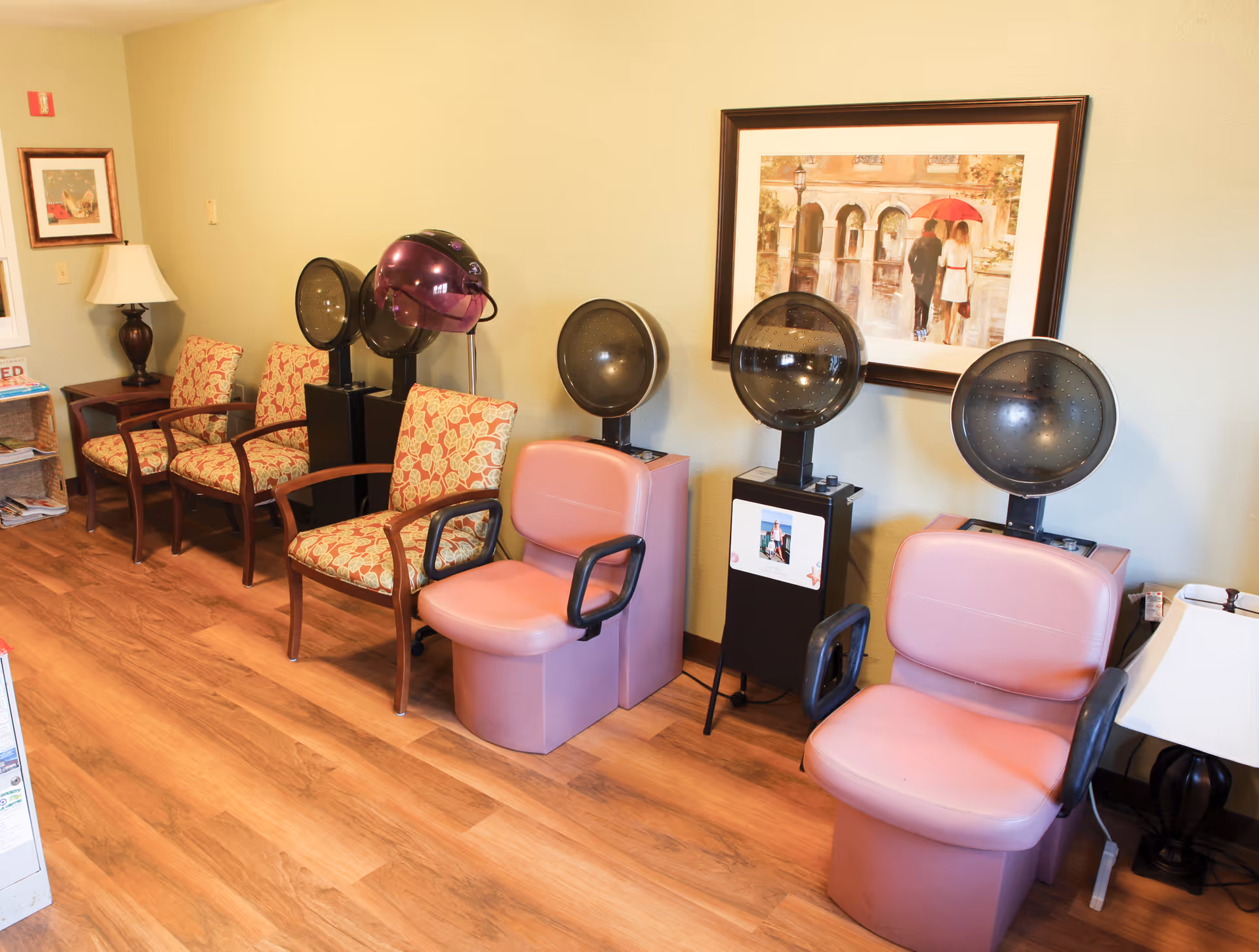Small salon area with pink hooded hair-dryer chairs and patterned waiting chairs along a wall.
