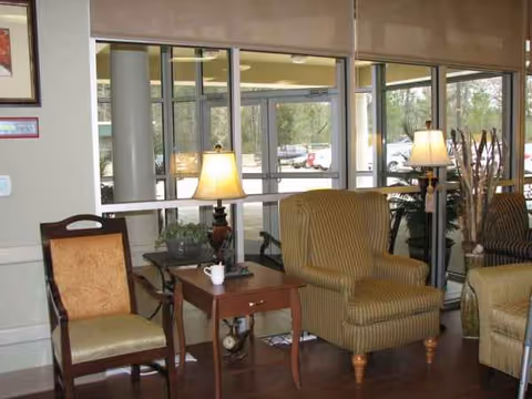 Cozy senior living lounge with lamps, armchairs, and a small table by large windows.