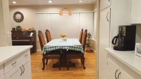 A dining room with a checkered tablecloth, six chairs, and warm wood floors.