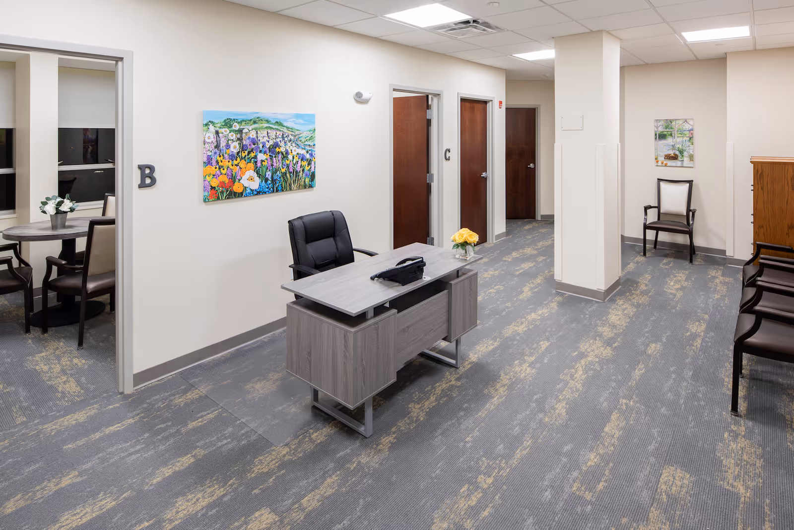 Reception area with a desk, office chair and waiting chairs in a clean hallway decorated with artwork.