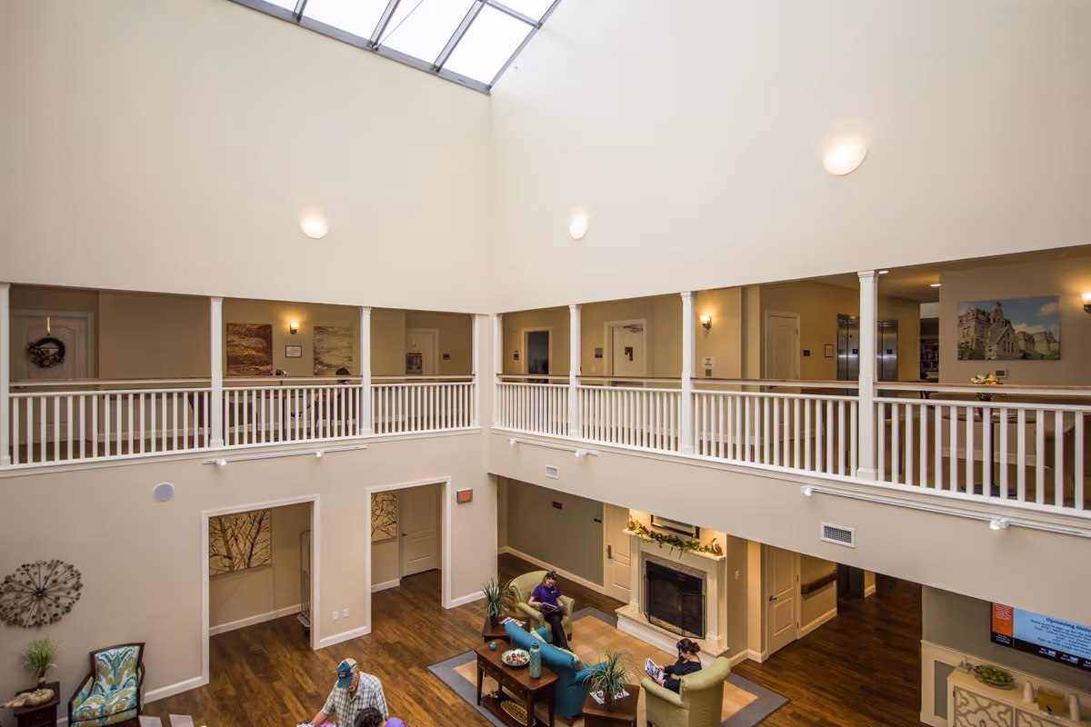 Two-story atrium lounge with seating around a fireplace, upper balcony railing, and a skylight overhead.