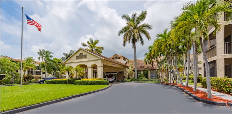 Exterior view of Waterside Landing senior living facility with palm trees and entrance drive.