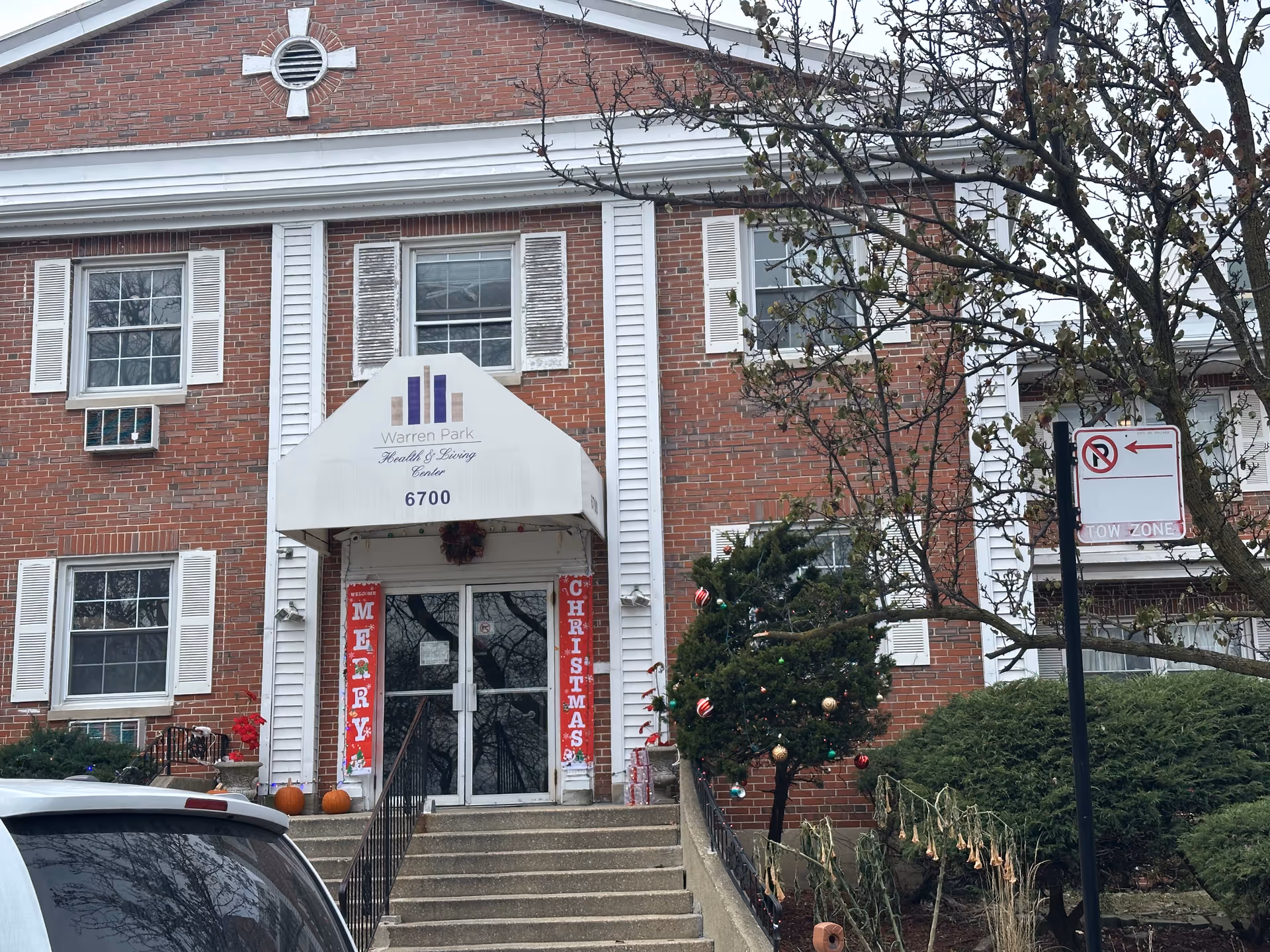 Brick façade and main entrance of Warren Park Health & Living Center showing an awning with '6700', steps leading up, and holiday decorations.