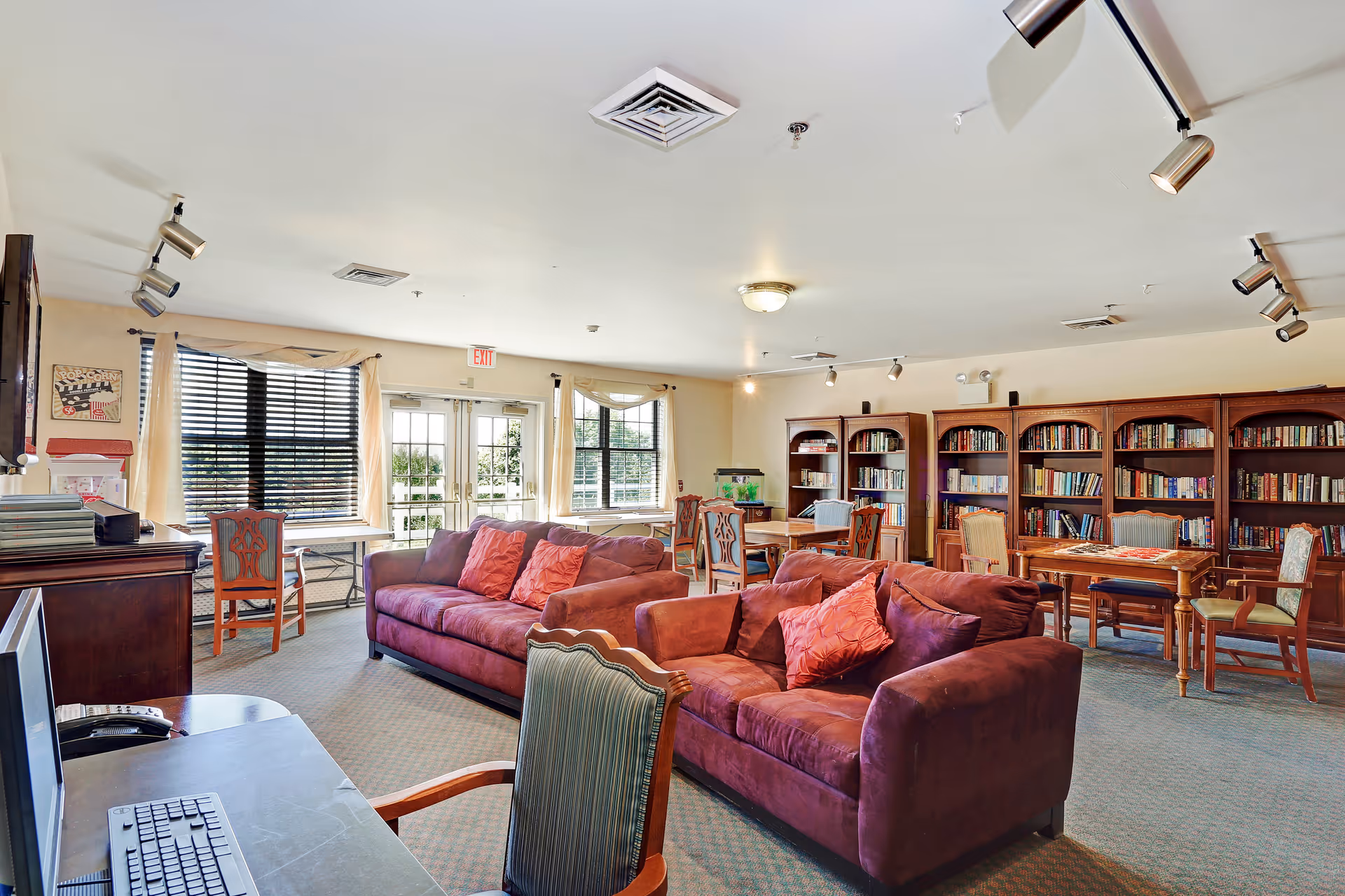 Spacious senior living common room with purple sofas, bookshelves, tables, and large windows letting in natural light.
