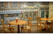 Interior of a dining area with wooden tables and chairs, featuring a wall mural depicting a quaint French street scene with storefronts including a boulangerie and a restaurant.