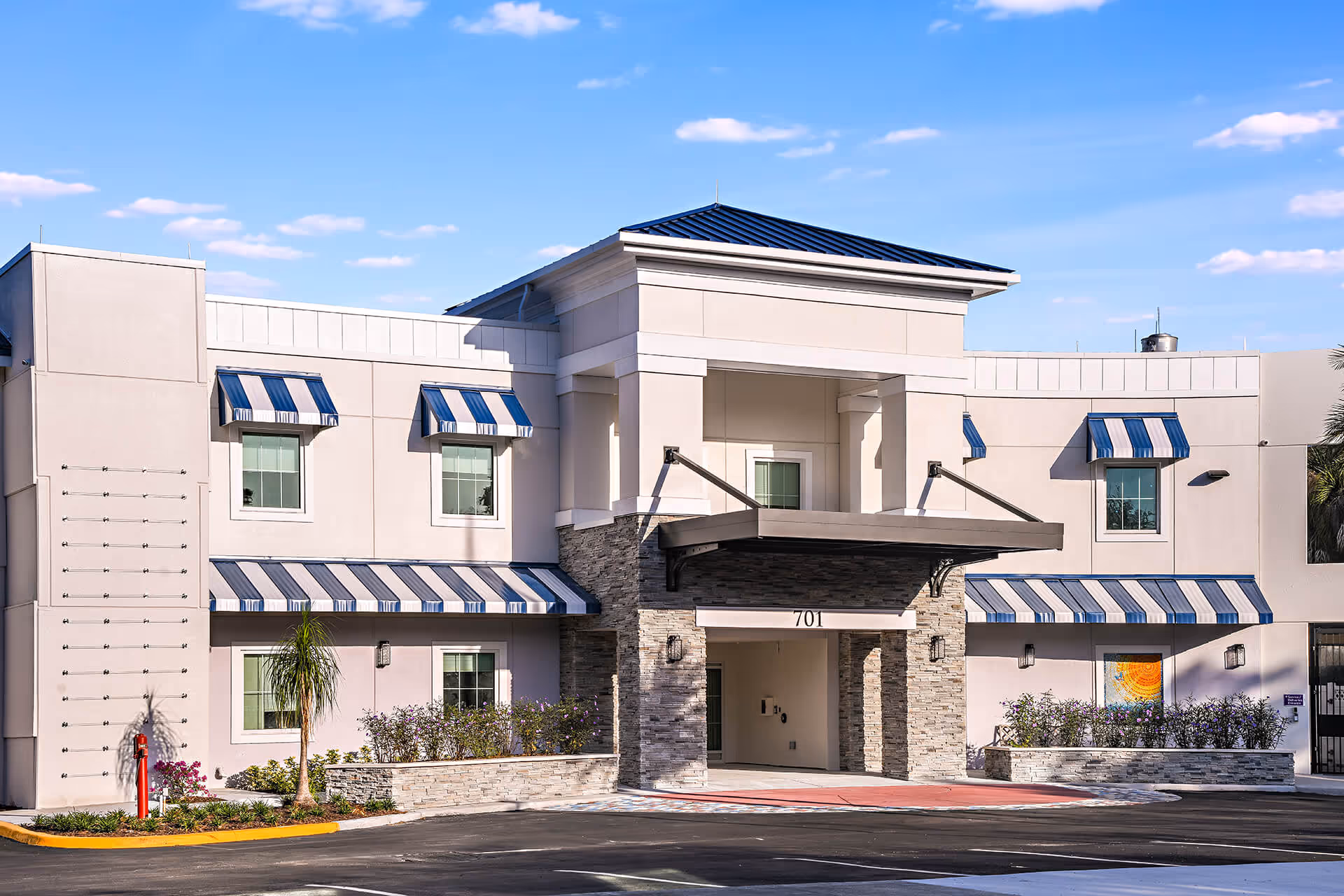 Modern beige senior living facility exterior with a stone entrance and blue striped awnings.