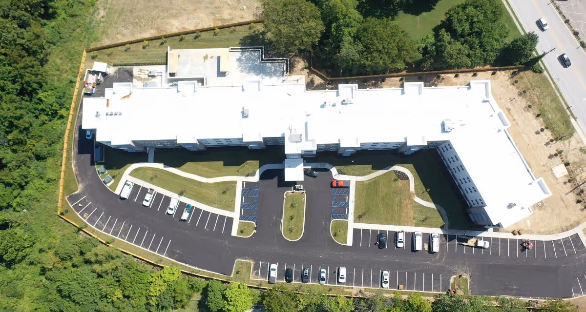 Aerial view of a large white-roofed senior living building with surrounding parking lots, driveways, and green landscaping.