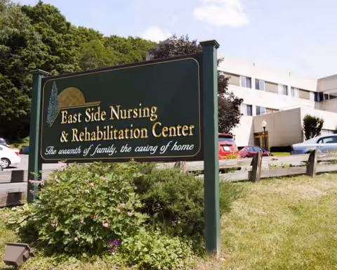 A green sign reading East Side Nursing and Rehabilitation Center in front of a beige building.