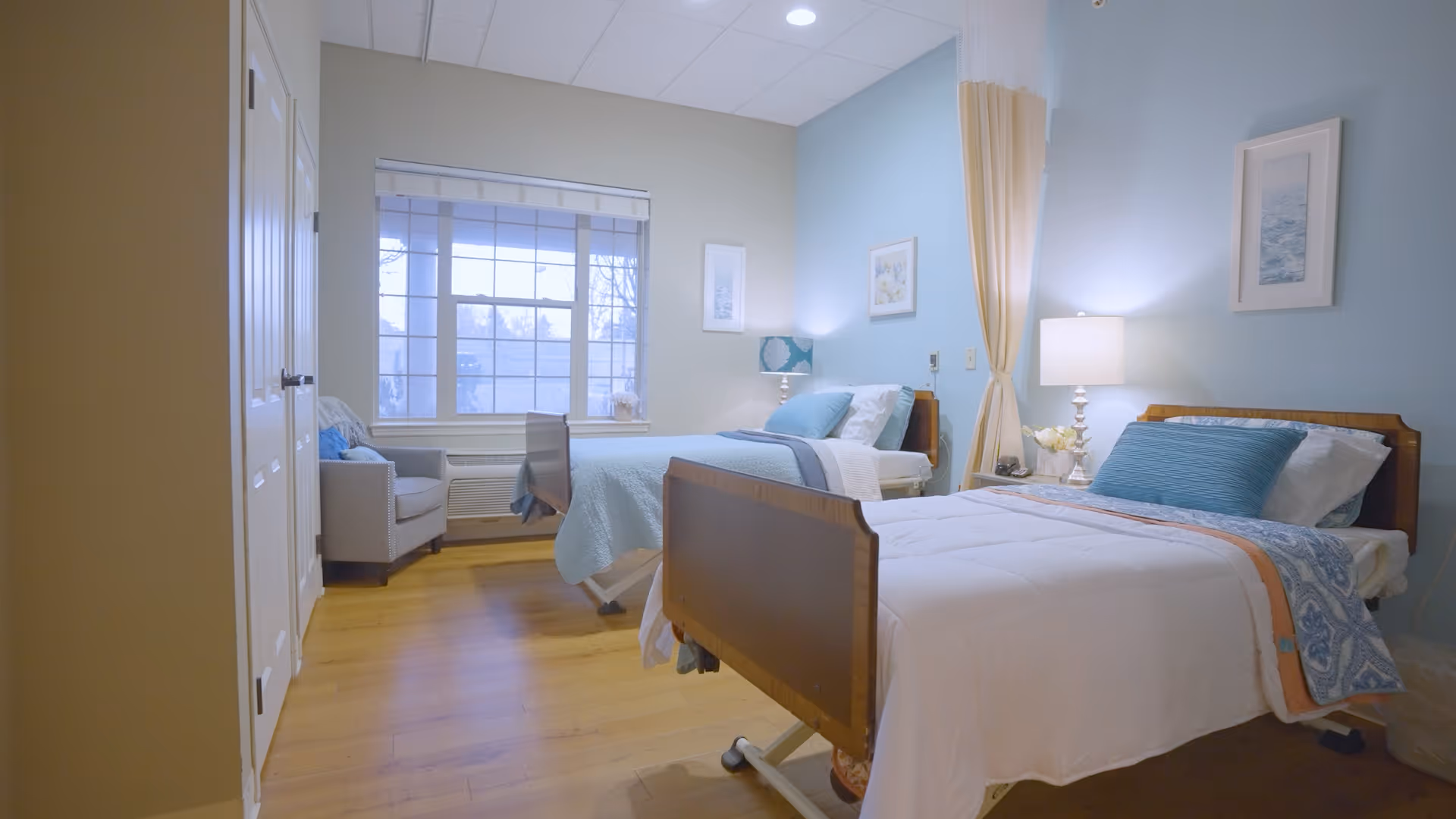 Shared bedroom with two twin beds, bedside lamps, a window, and an armchair.