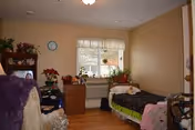 Small bedroom with two beds, dresser, and window in soft lighting.