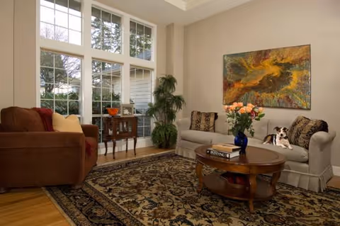 Evergreen Elderly Care I living room with two sofas, coffee table, rug, plants, and a dog.