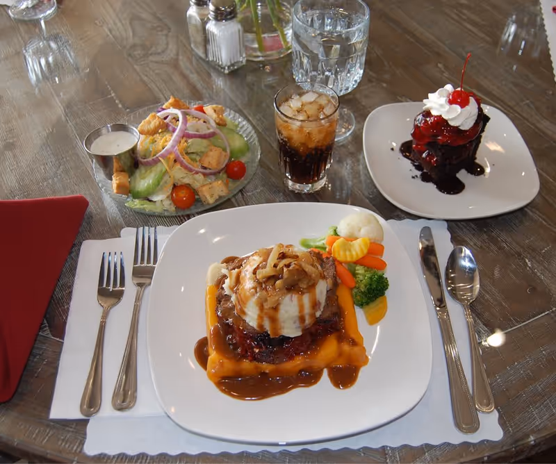 Plated entrée with mashed potatoes, vegetables, a side salad, dessert and drinks set on a dining table.