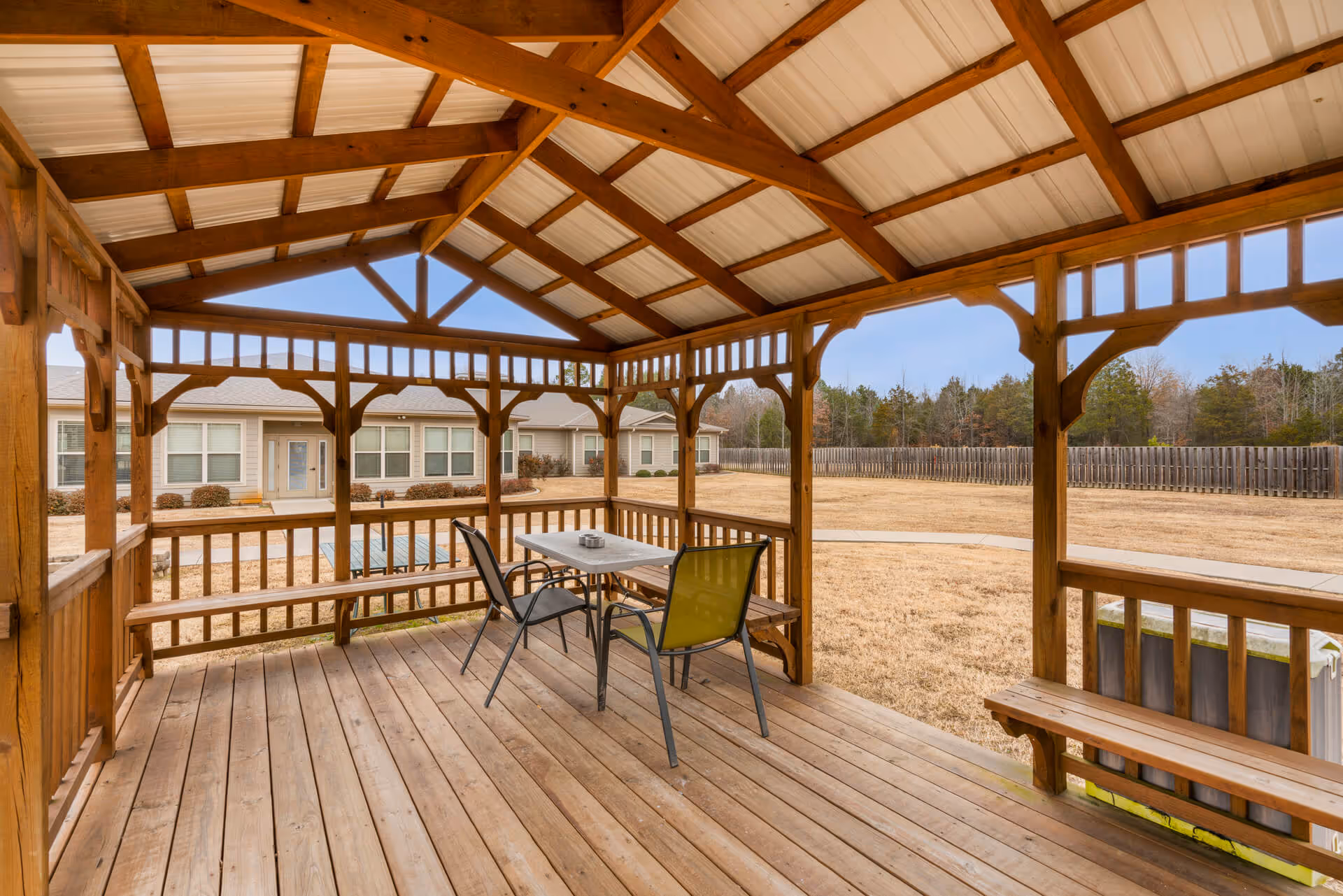 Wooden gazebo with a table and chairs overlooking a lawn and nearby single-story senior living buildings.