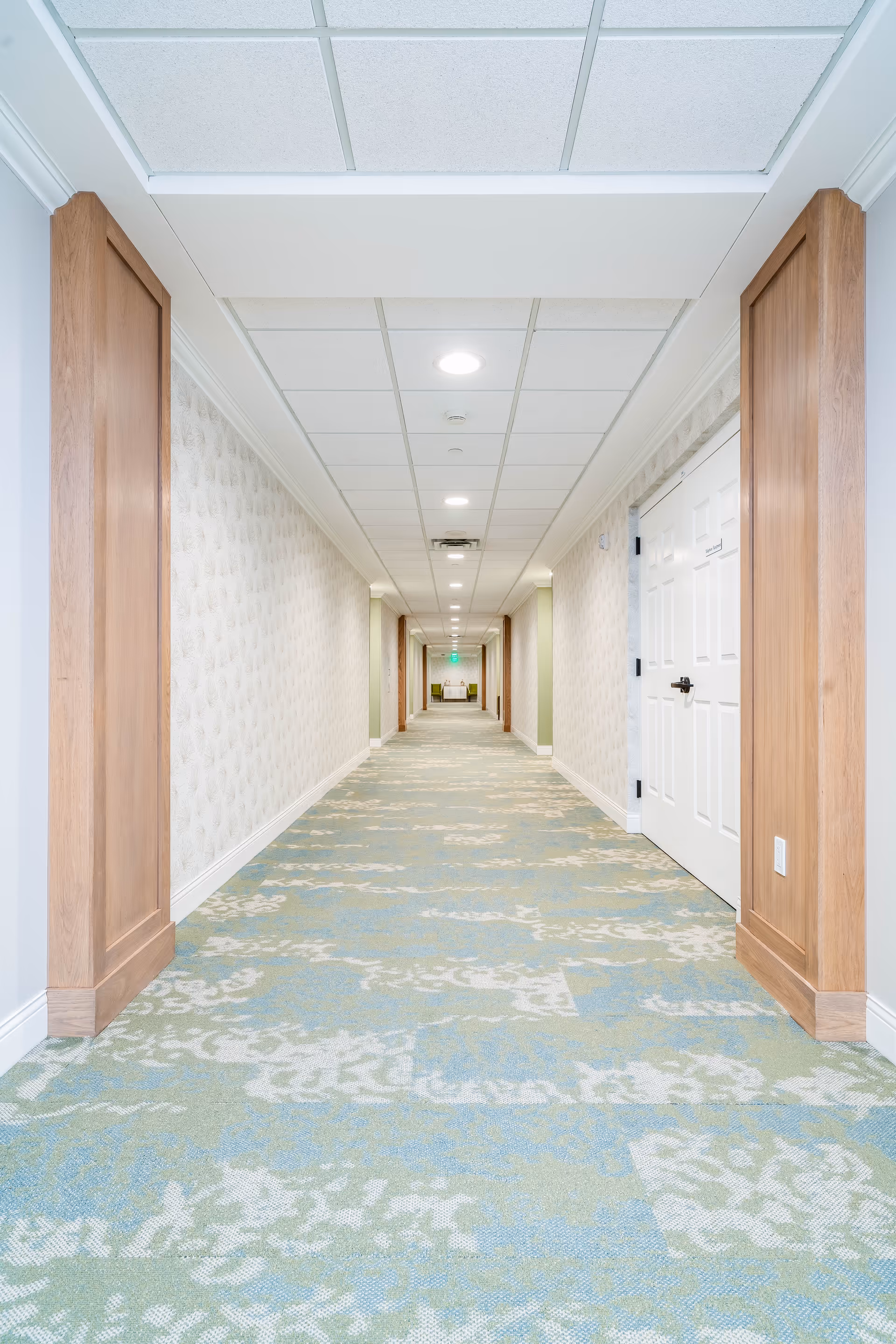 A long hallway in a senior living facility with patterned carpet and doors on either side.