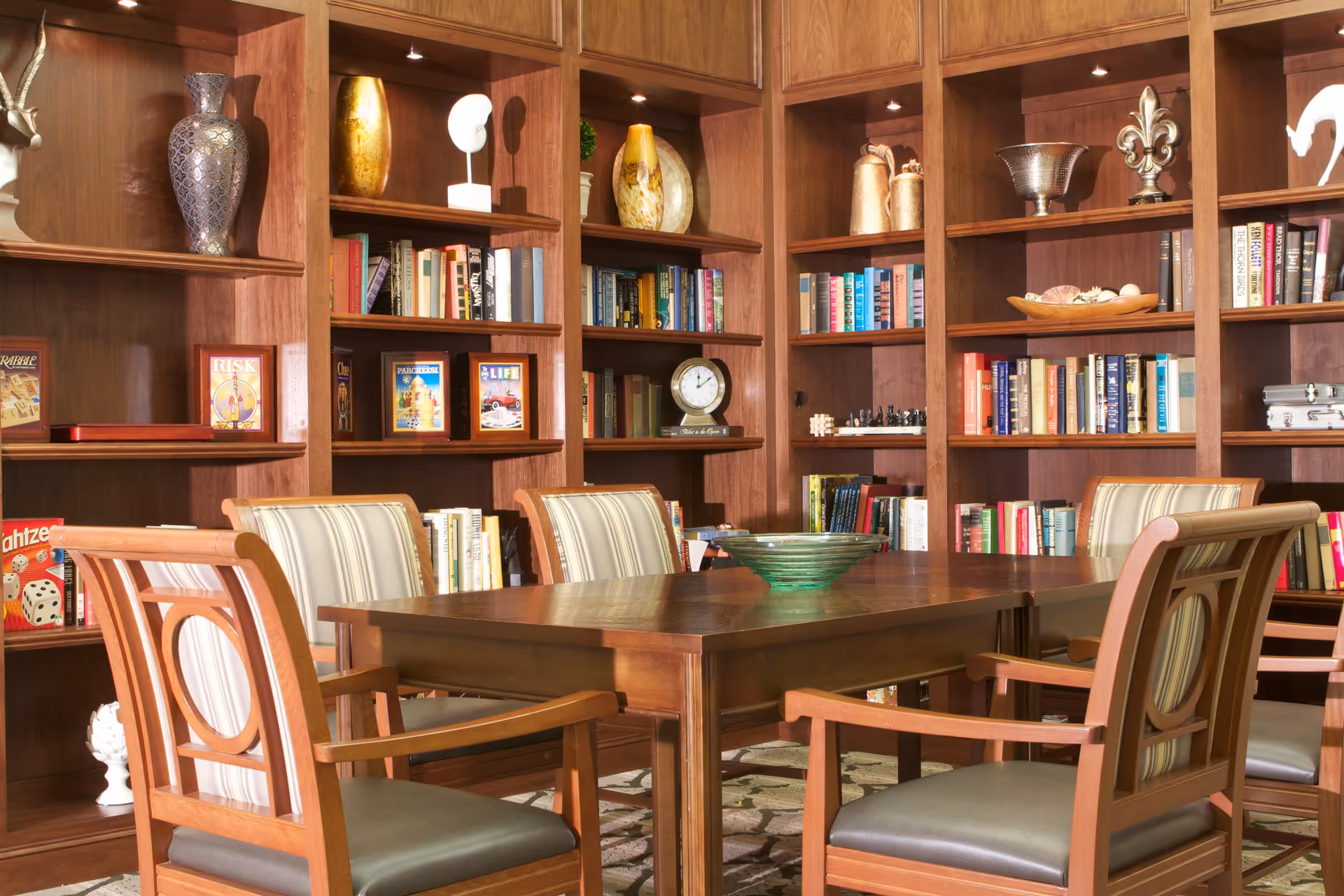 Wood-paneled library-style room with bookshelves, a wooden table and upholstered chairs.
