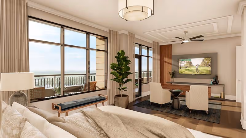 Spacious bedroom suite with a bed in the foreground, seating area and wall-mounted TV, and large windows opening to a balcony.