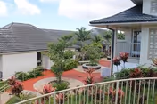 Outdoor courtyard with circular planter, red walkways, tropical plants, railings, and surrounding two-story buildings with tiled roofs.