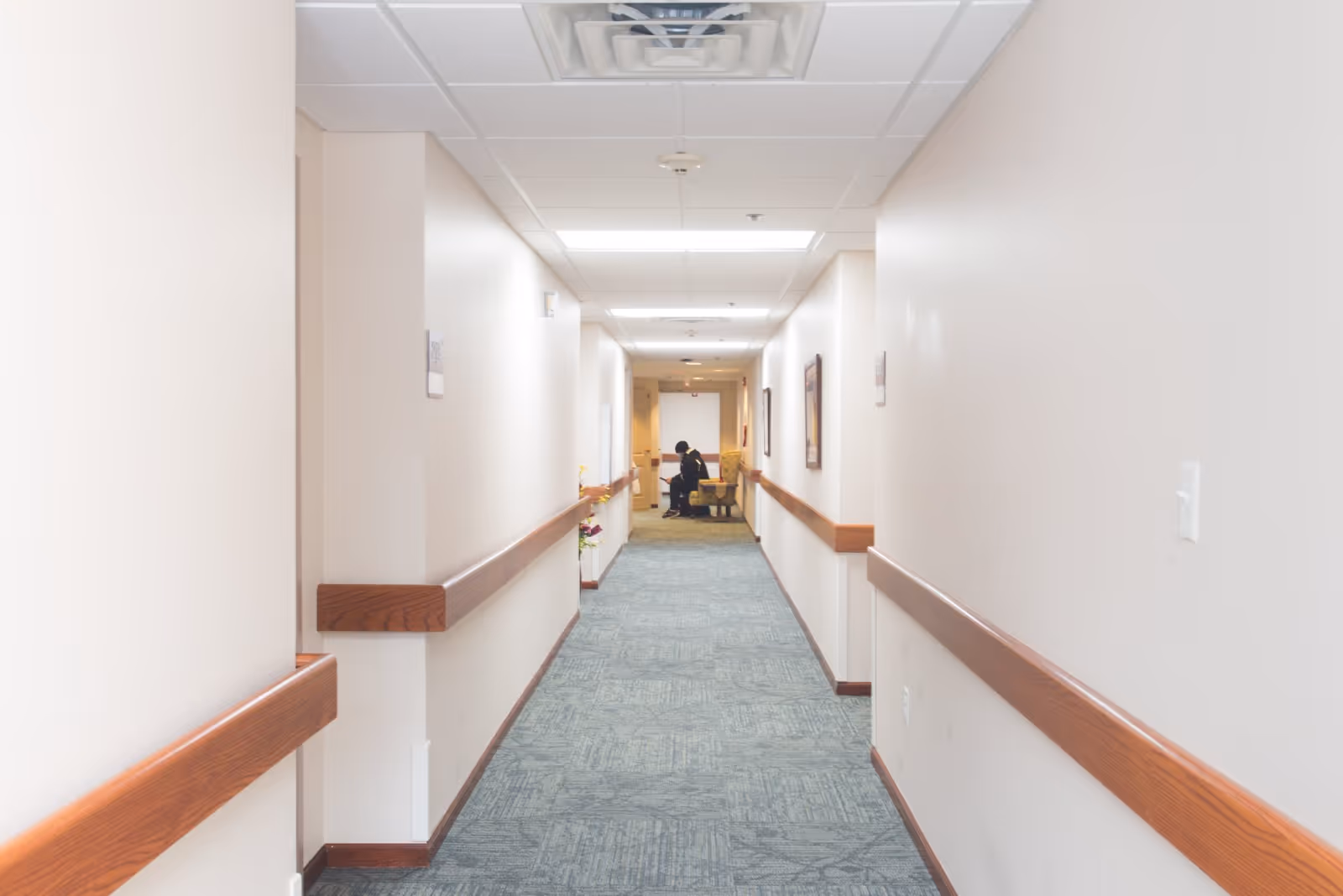 Bright, carpeted interior hallway with wooden handrails leading to a seating area at the far end.