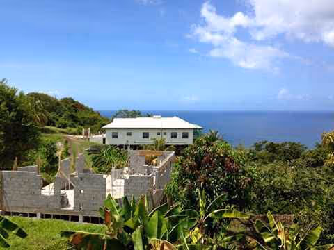 White building on a hilltop with ocean view and lush tropical plants.