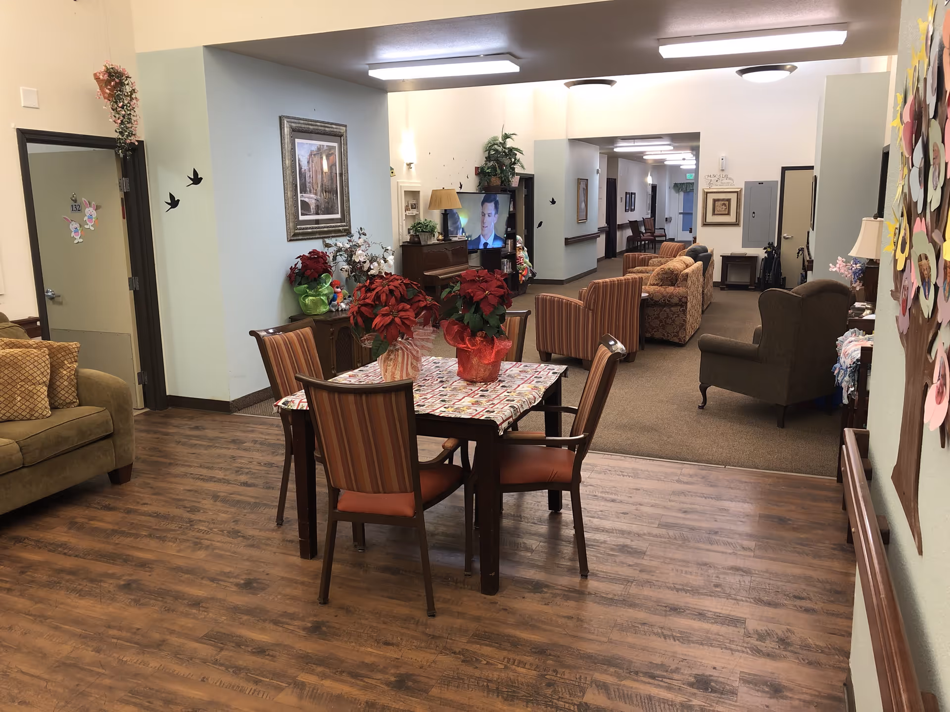 Interior common area with a dining table and chairs in the foreground and a lounge with sofas, armchairs and a TV in the background.