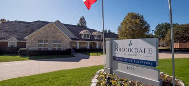 Front entrance of Brookdale Tyler East senior living building with a sign, driveway, and landscaped lawn under a clear sky.