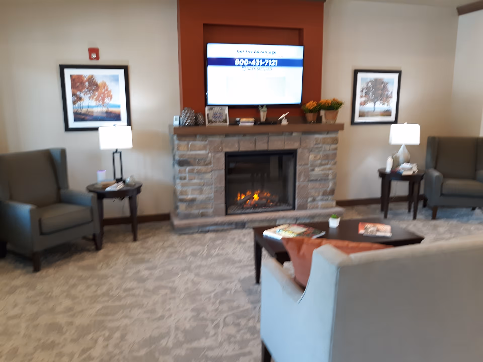 Cozy communal living room with a stone fireplace, wall-mounted TV, armchairs, a sofa and side tables.