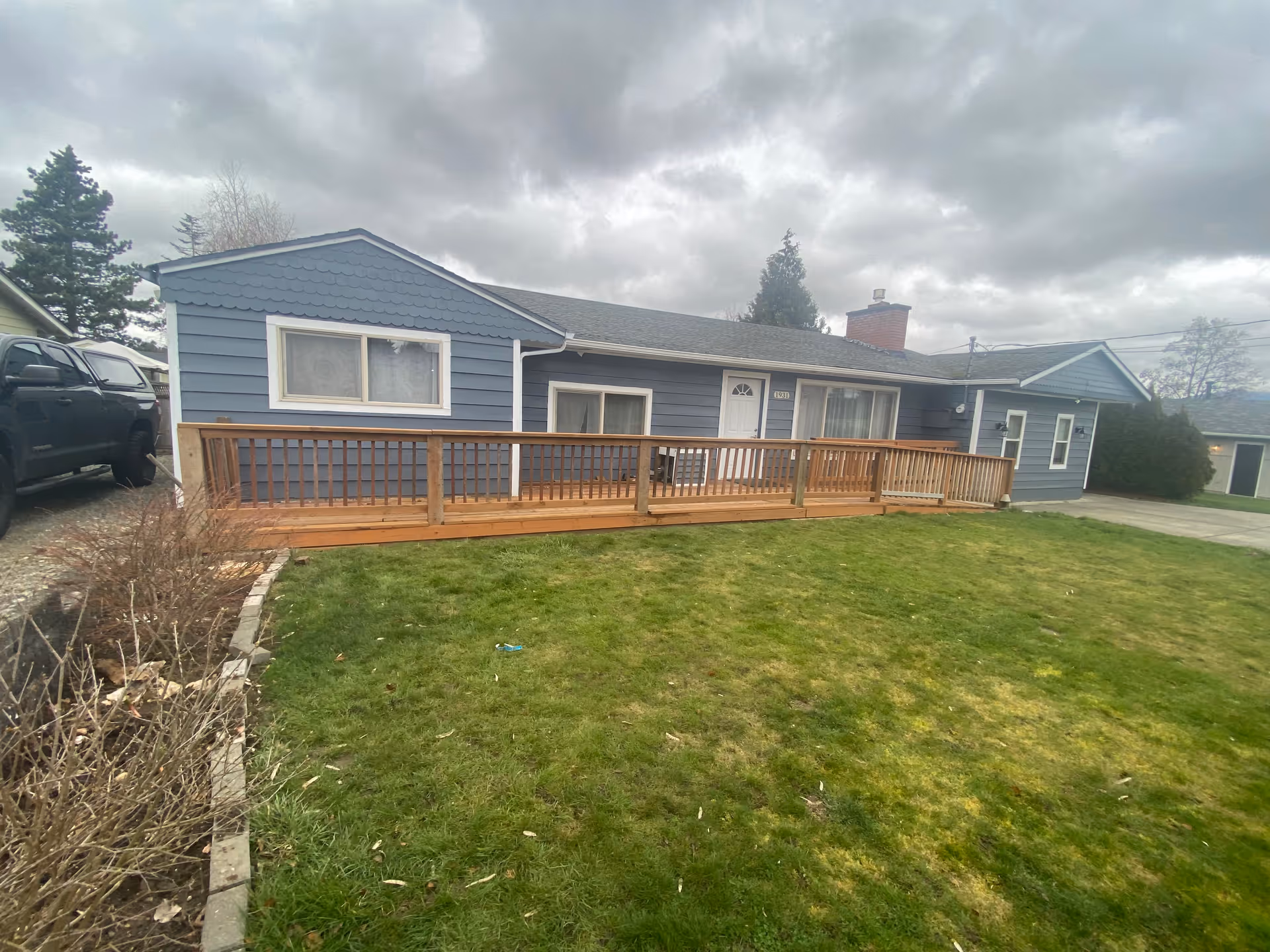 Single-story blue house with a wooden front ramp and a grassy lawn under a cloudy sky.