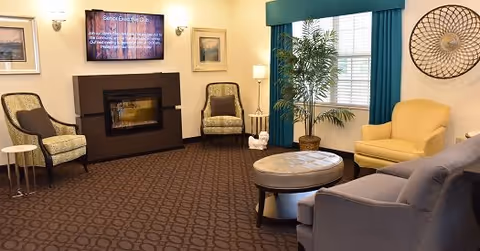 A comfortable sitting room with armchairs, a sofa, coffee table, fireplace, wall-mounted TV and a potted plant by the window.