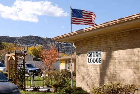 Exterior view of Canon Lodge Care Center with American flag, brick façade, and landscaped entry.