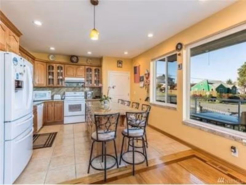 Bright kitchen with a central island and bar stools beside large windows overlooking the outside.