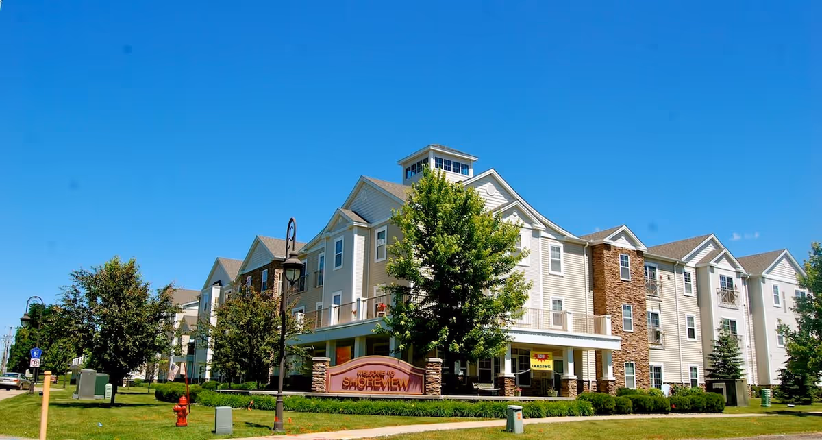 Exterior view of a multi-story senior apartment building named Shoreview with a well-maintained lawn, trees, and a clear blue sky.