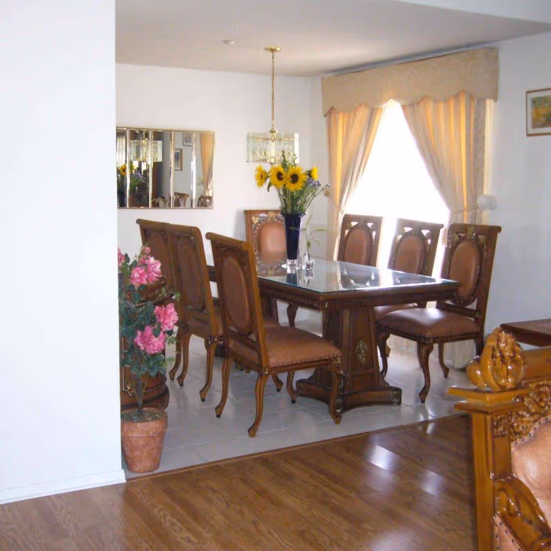 Elegant dining room with a glass-topped table, wooden chairs, and sunflowers as centerpiece.