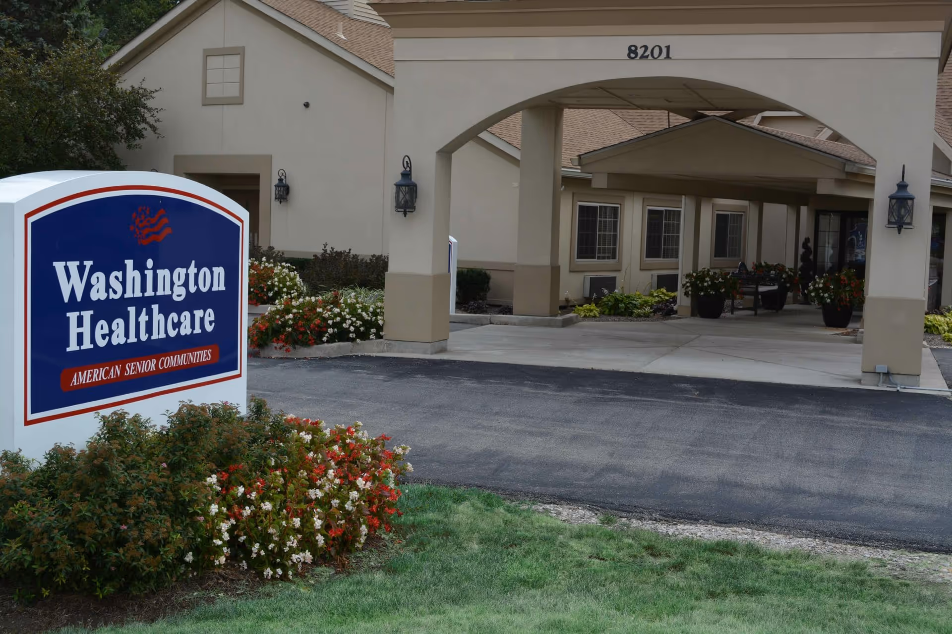 Front entrance of Washington Healthcare senior living facility showing the driveway, covered entryway, landscaping, and a sign reading "Washington Healthcare".