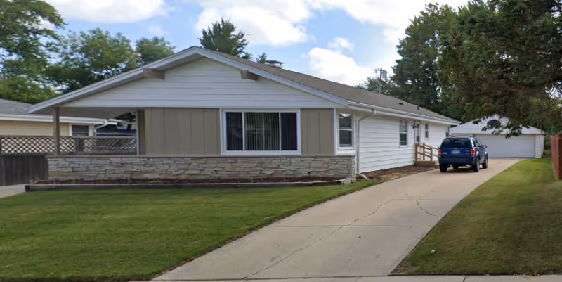 Single-story residential-style facility with stone facade, driveway, and a blue SUV parked outside.